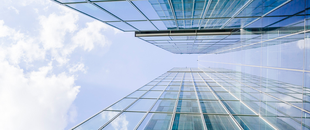 Glass office towers viewed from below against a bright sky representing MetLife Investment Management’s investment grade corporate market outlook.
